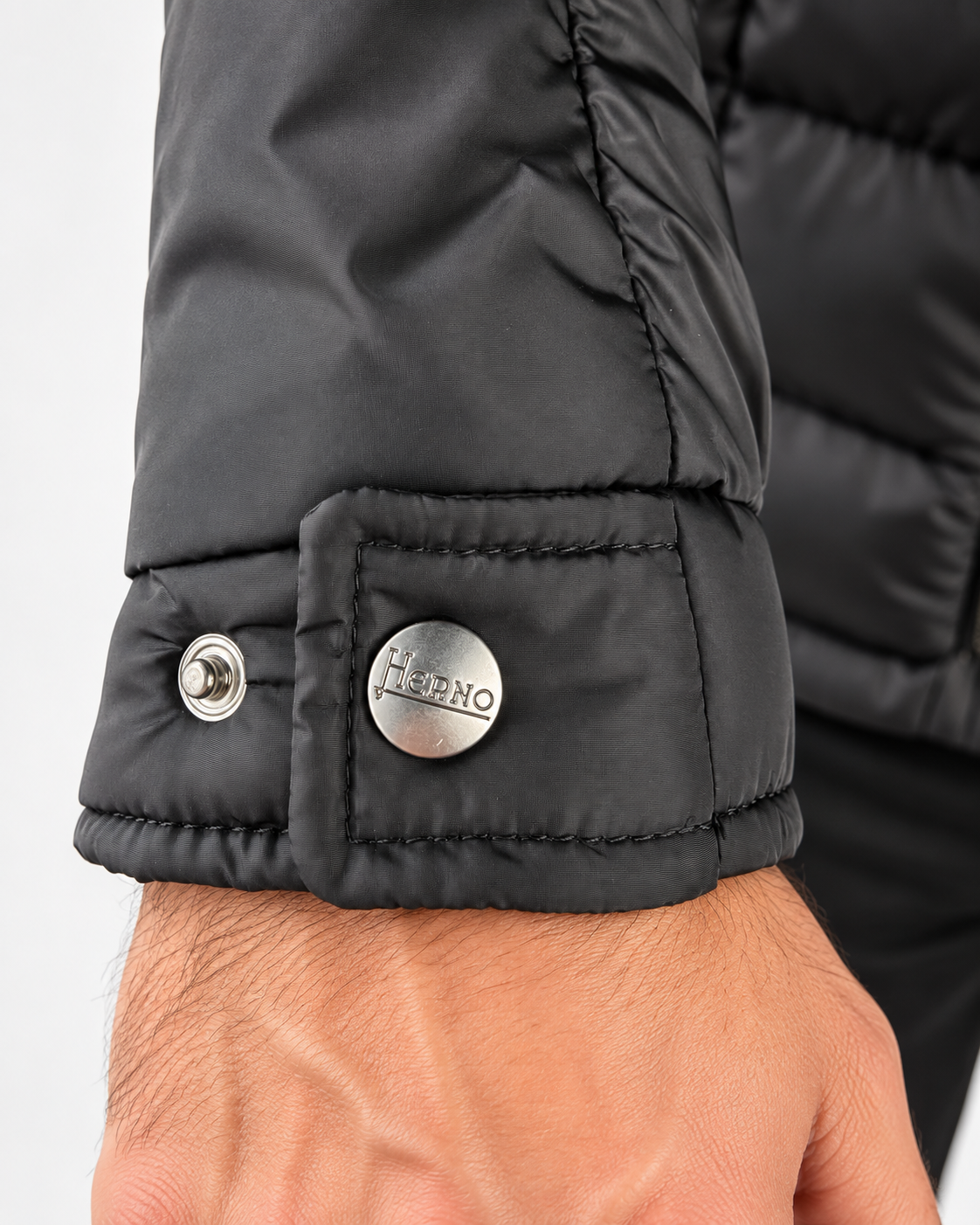 Dettaglio del polsino nero con cinturino di regolazione e bottoni a pressione metallici firmati Herno.